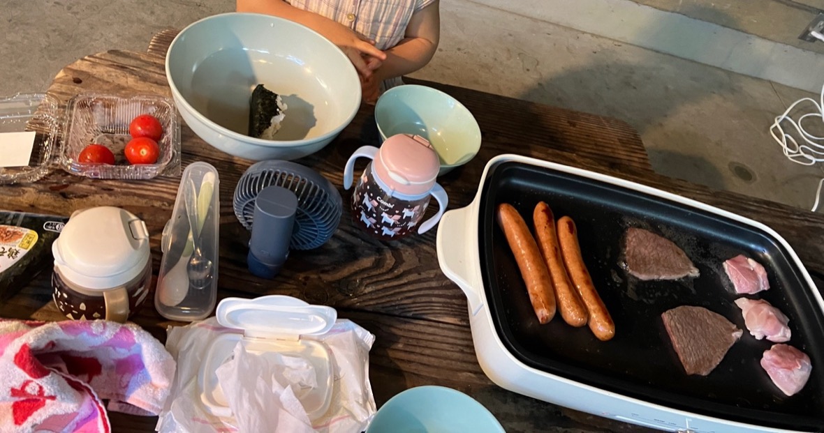 ホットプレートでウインナーと肉を焼く。テーブルにはストローマグとベビー用スプーン、おしりふき