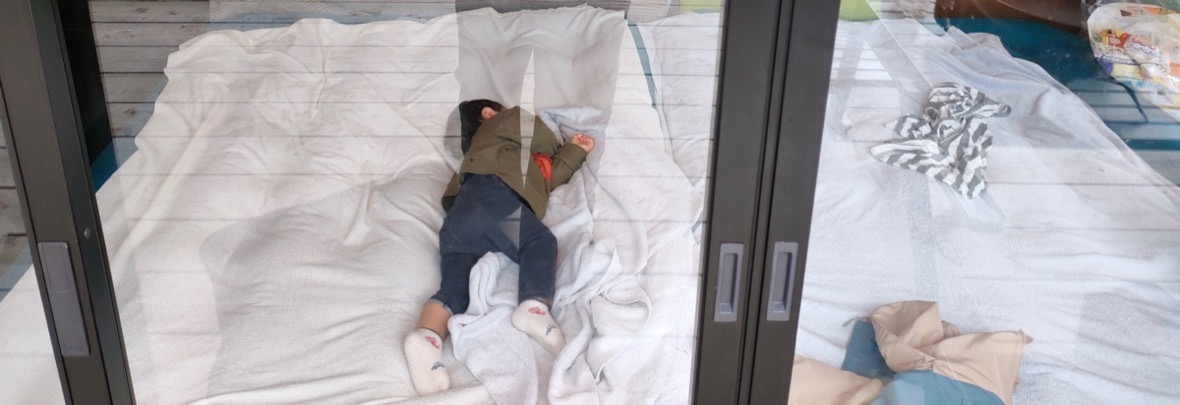 コテージの床に敷いたマットの上で、うつぶせで眠る子ども
