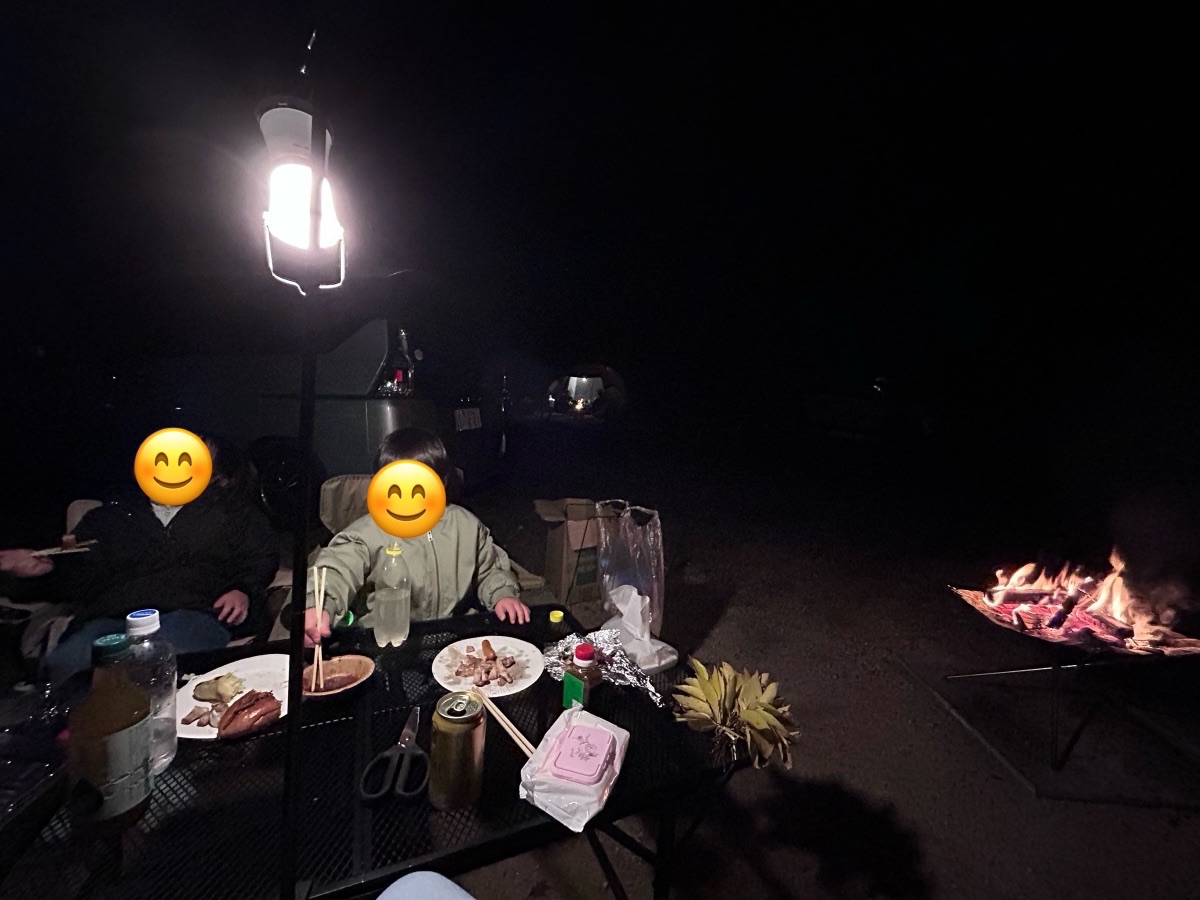 夜、ランタンの下で上着を着た子ども2人が夜ごはんを食べているところ