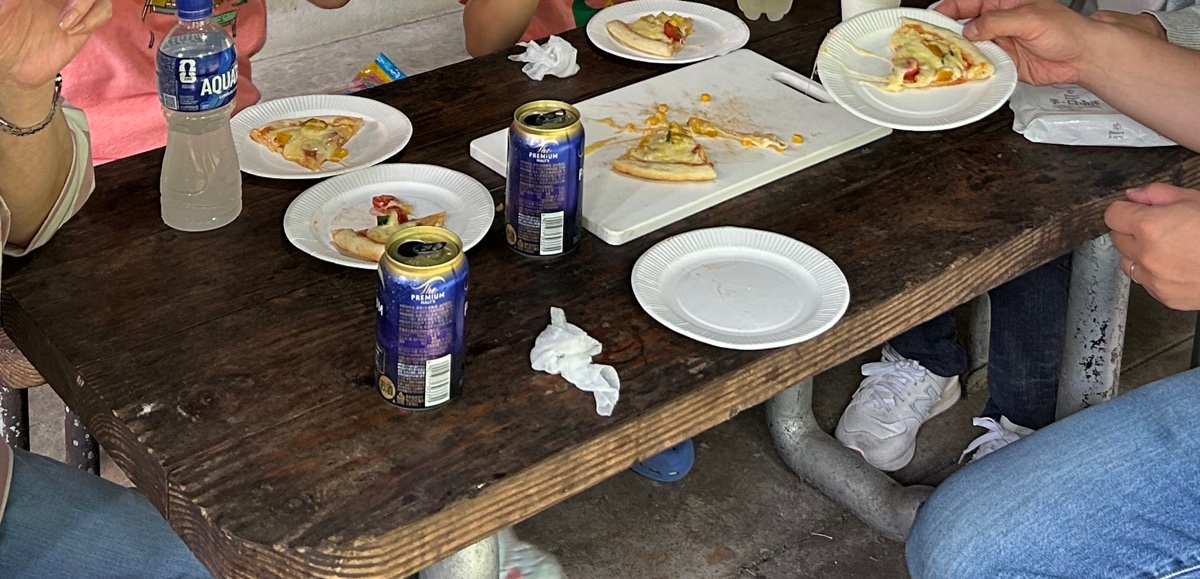 屋外のテーブルで、みんなで焼いたピザを食べているところ