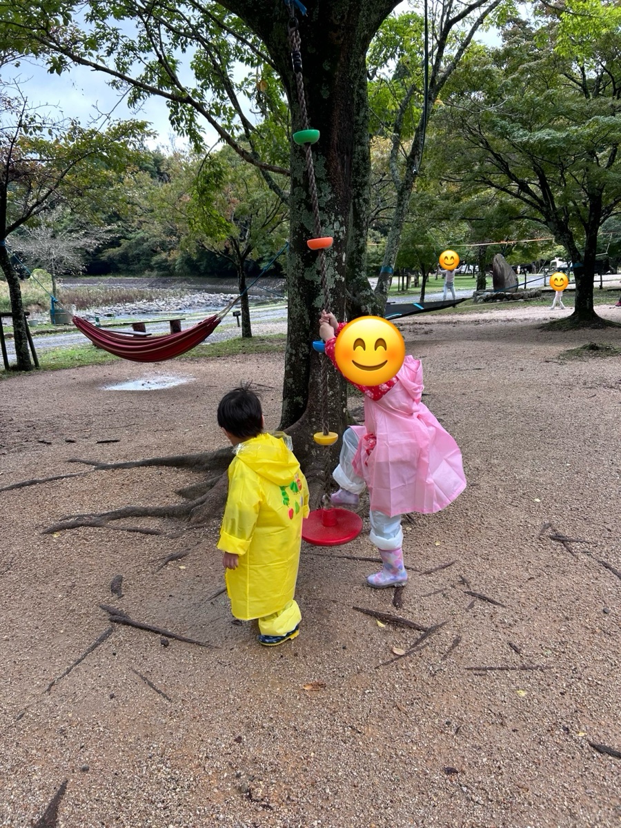 カッパと長靴姿の子ども2人が、木のそばで遊んでいるところ