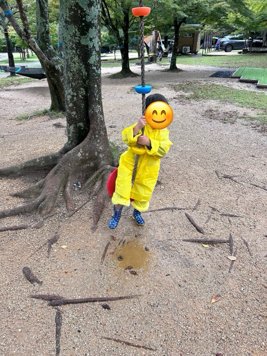 黄色いカッパを着た子どもが、ロープのブランコに乗っているところ