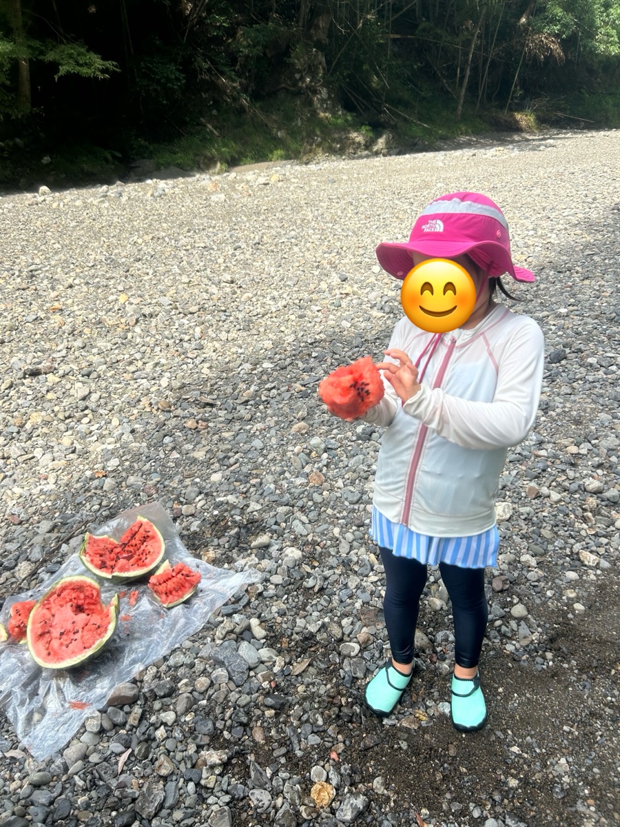 割ったスイカを川原で食べる子ども