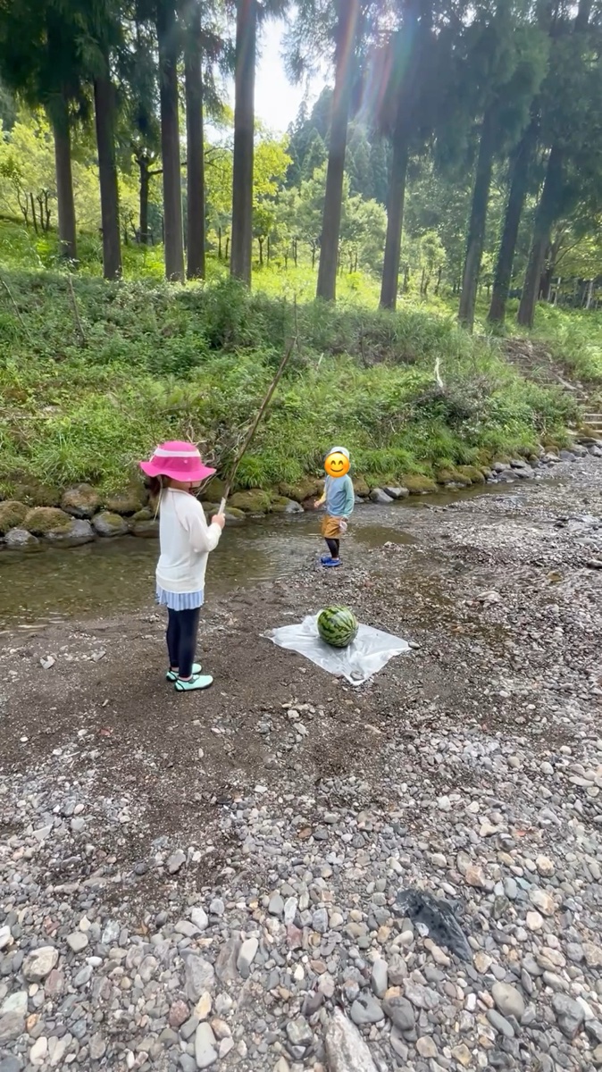 川原でスイカ割りをする子ども。棒を持って狙いを定めているところ