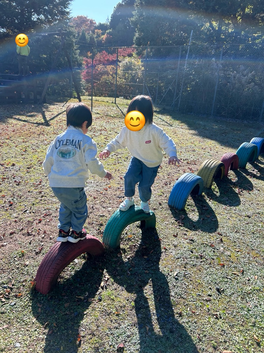 地面に半分うまった色とりどりのタイヤの上を歩く子ども2人