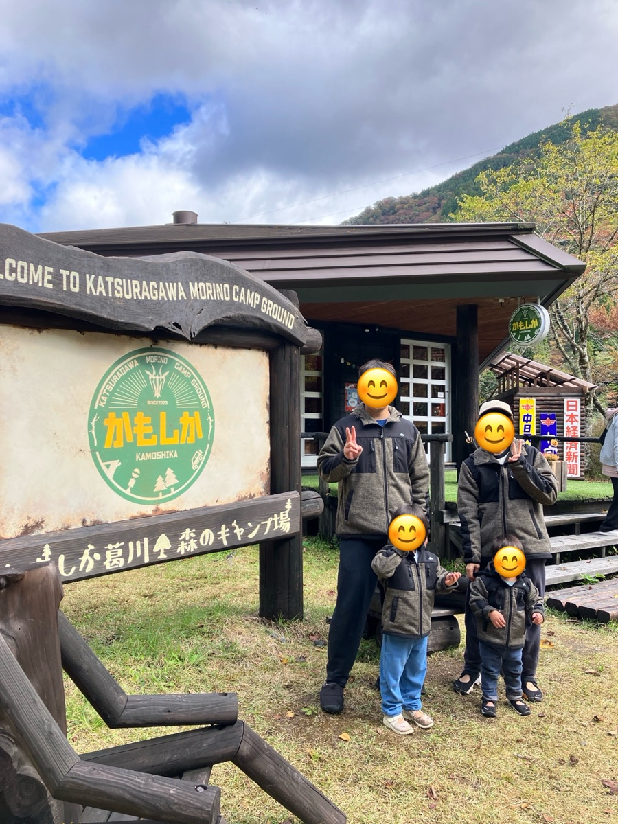 キャンプ場の看板の前に立つ家族4人