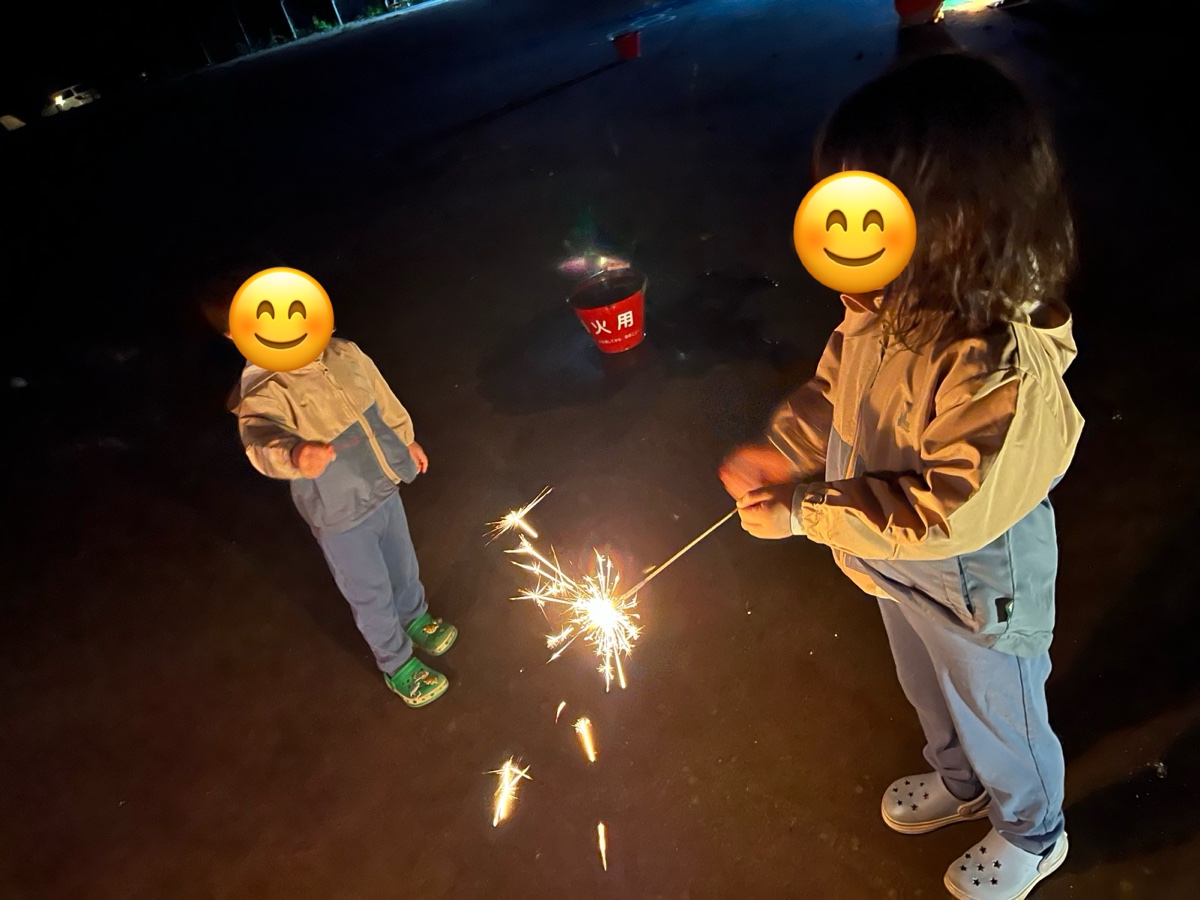 夜に手持ち花火をする子ども2人と、奥にある花火用のバケツ