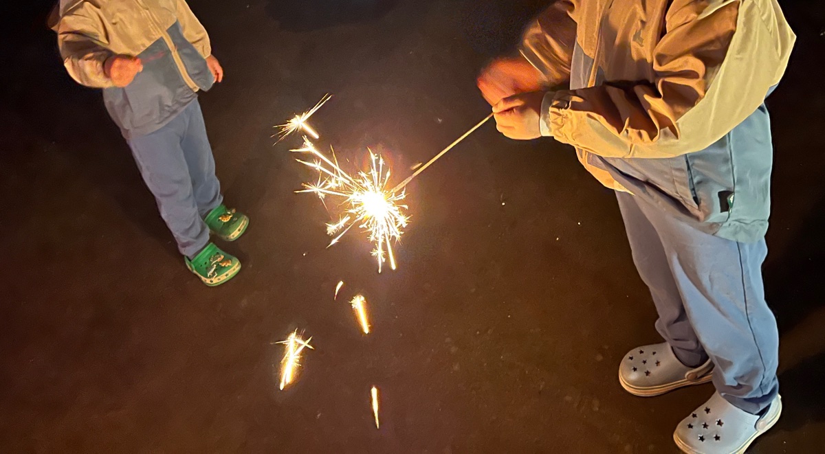 夜のキャンプ場で、手持ち花火をする姉と弟の手元